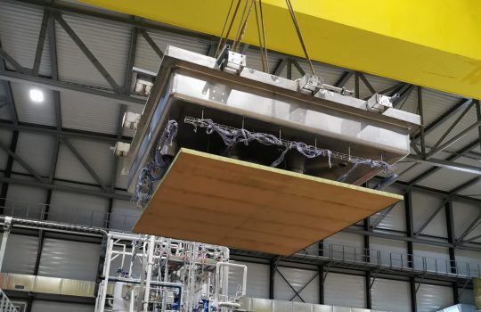 A large, flat piece of equipment being lowered by a crane